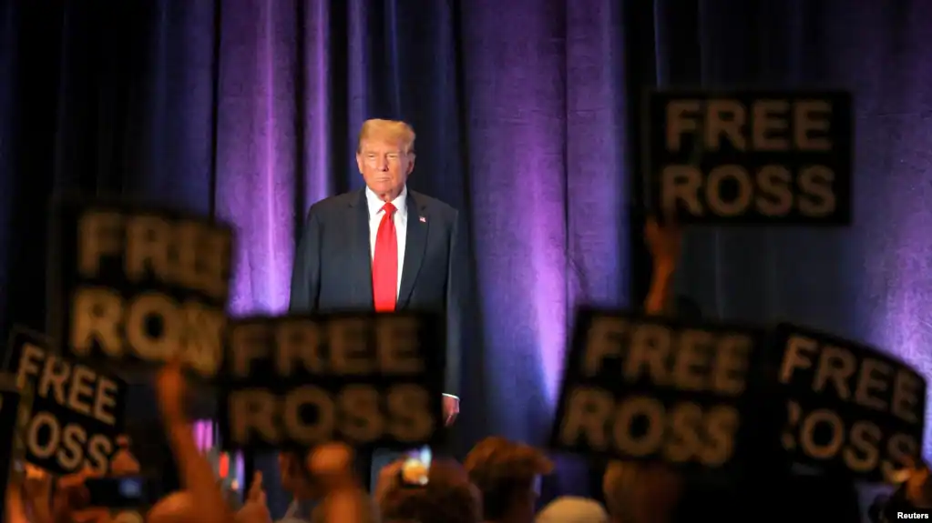 Multitud sostiene carteles en apoyo a Ross Ulbricht en mitin de Trump.